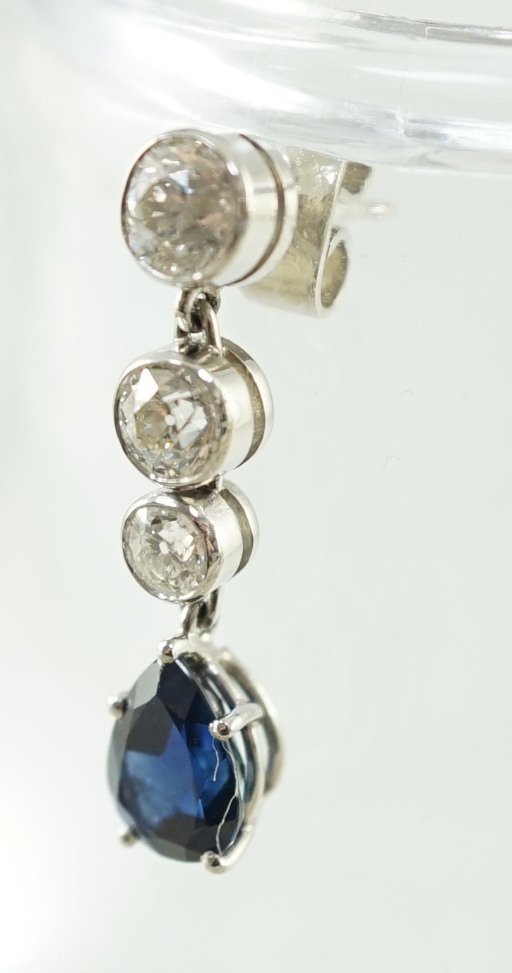 A pair of 1980's platinum, single stone pear cut sapphire and graduated three stone collet set diamond drop earrings